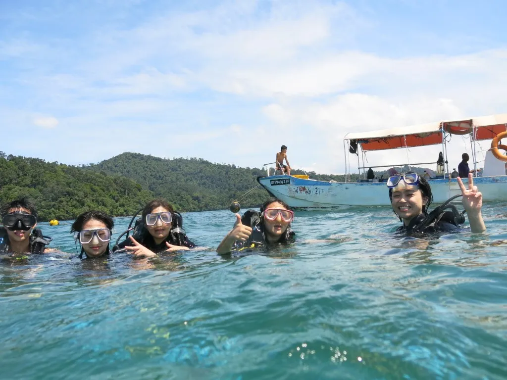 A group of smiling divers at the surface in front of a dive boat